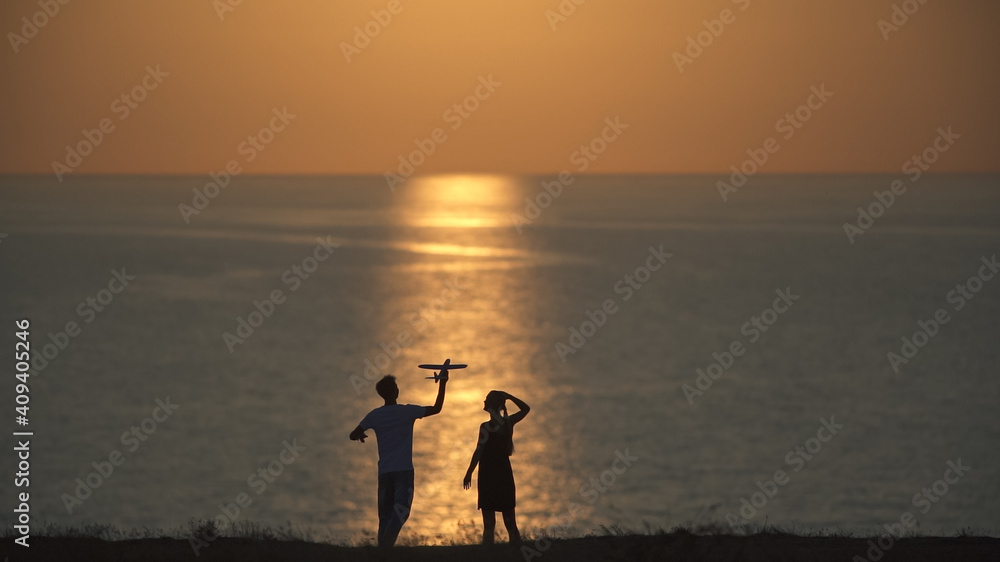 The man and woman launch a toy plane on the sea sunset bakcground