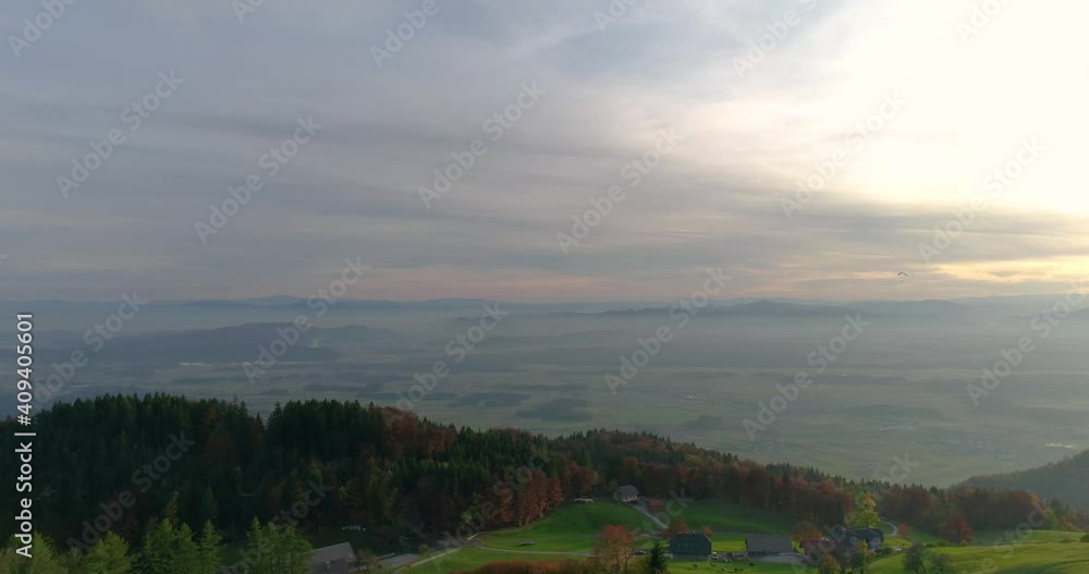 Drone flying over grassland slope in Slovenia. High altitude village and large basin in the distance. Beautiful sunset over Alps mountains. Aerial view of beautiful, fairy tale landscape. Dynamic Drone flying over grassland slope in Slovenia. High altitude village and large basin in the distance. Beautiful sunset over Alps mountains. Aerial view of beautiful, fairy tale landscape. Dynamic