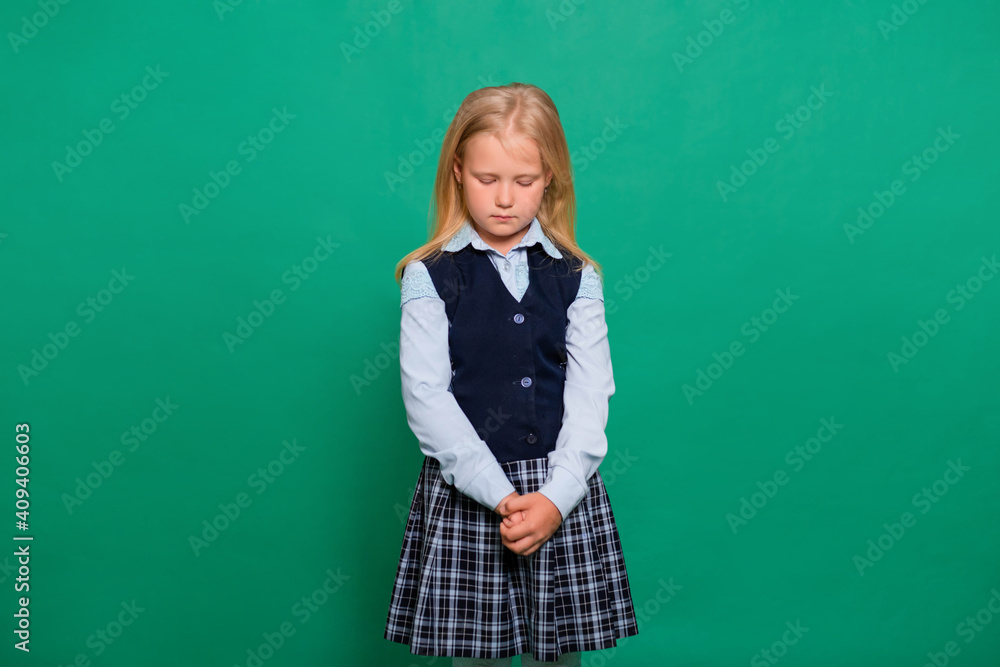 Shy schoolgirl looks down isolated on a green background.