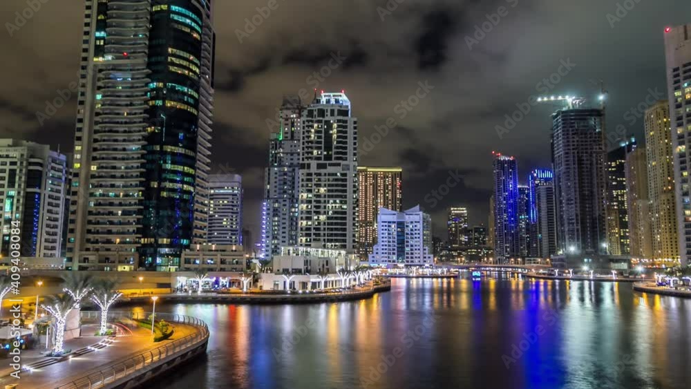 Dubai Marina promenade with yachts and modern towers reflected in water from waterfront night timelapse hyperlapse, United Arab Emirates. District with artificial canal and illuminated skyscrapers Dubai Marina promenade with yachts and modern towers reflected in water from waterfront night timelapse hyperlapse, United Arab Emirates. District with artificial canal and illuminated skyscrapers