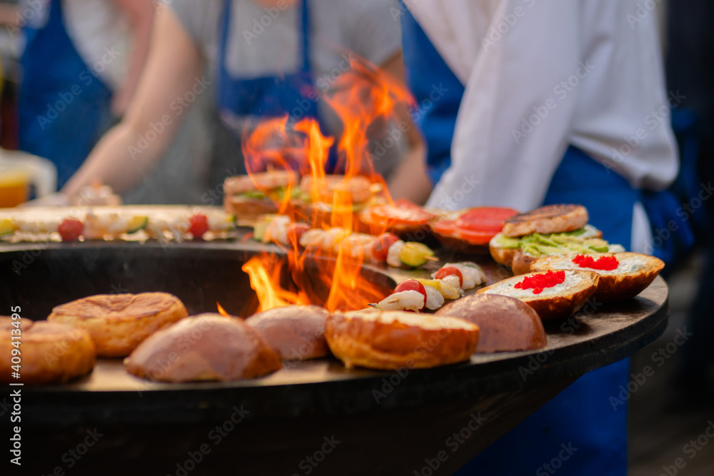 Preparing shrimp, prawn skewers and burgers with red caviar, avocado on brazier with hot flame at summer local food market - close up. Outdoor cooking, seafood, gastronomy, street food concept