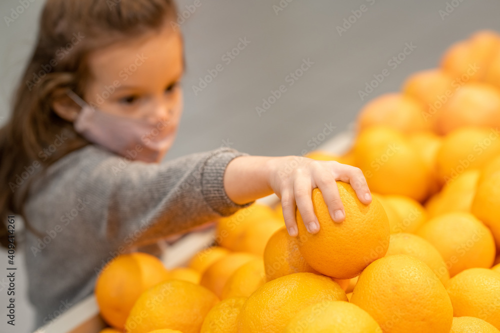 Hand of cute little girl in casualwear and protective mask taking fresh orange Hand of cute little girl in casualwear and protective mask taking fresh orange