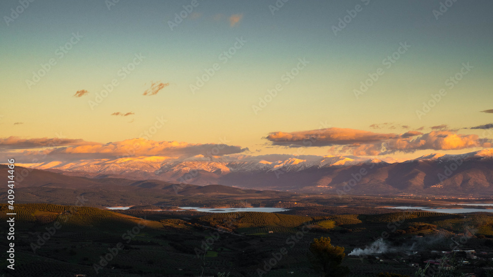 countryside landscape with snowy mountains and clouds at sunset