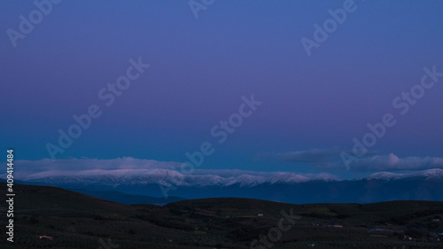 countryside landscape with snowy mountains and clouds at sunset with purple hues reaching blue hour © Rocio