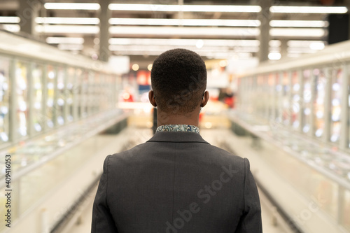 Rear view of young African businessman moving between displays with frozen food