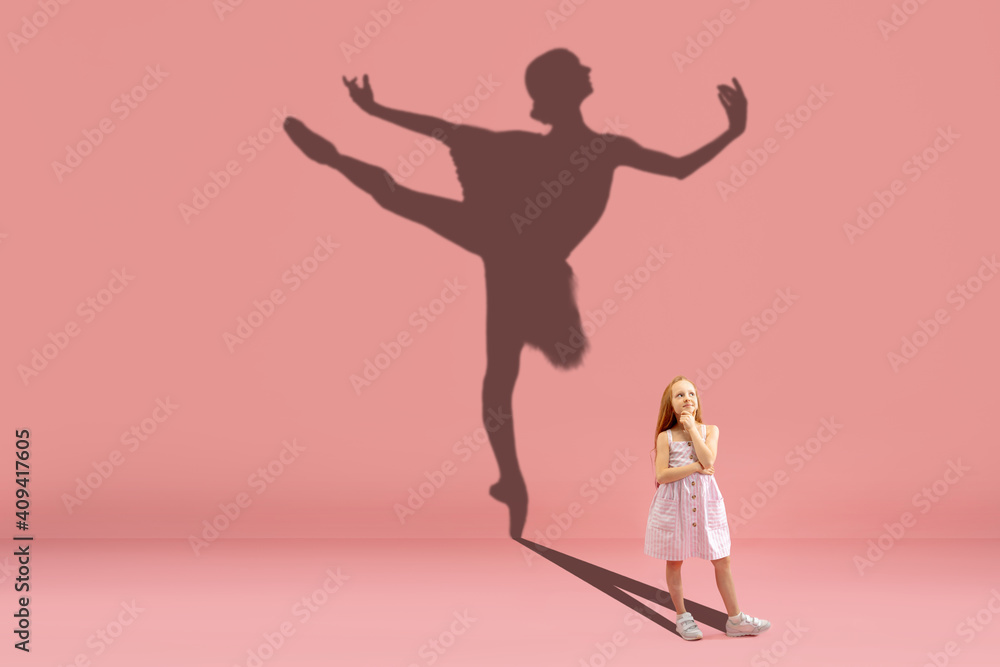 Childhood and dream about big and famous future. Conceptual image with girl and drawned shadow of ballerina dancing on coral pink background. Childhood, dreams, imagination, education concept.