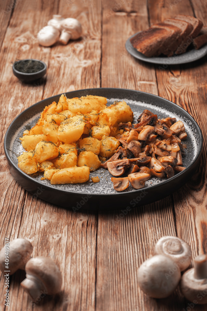 Fried potatoes with mushrooms on a gray plate next to fresh mushrooms Fried potatoes with mushrooms on a gray plate next to fresh mushrooms