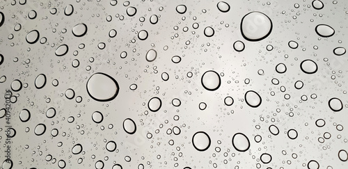 Rain drops or water droplets on clear glass on a gray background. 