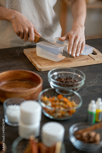Hands of female standing by table and cutting hard soap mass on wooden board