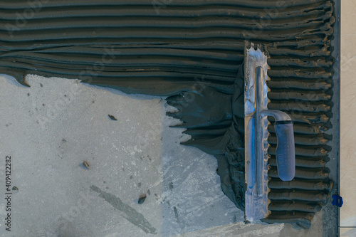 Close up of the hands of a master builder's man with a notched trowel, putting a tile adhesive mixture, performs the installation of ceramic tiles