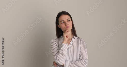 Pensive puzzled young businesswoman touching chin, looking up in distance, thinking of problem solution or pondering difficult decision, feeling doubtful isolated on white wall or studio background.