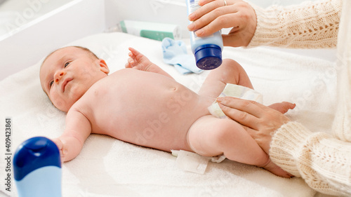 Фотография Little newborn baby lying on changing table while mother changing diaper and applying talc on soft skin