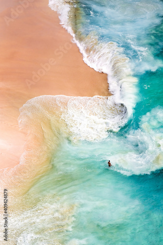 View from above, stunning aerial view of a person relaxing on a beautiful beach bathed by a turquoise sea during sunset. Kelingking beach, Nusa Penida, Indonesia.