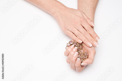 Beautiful Female well-groomed Hands with French manicure holding necklace over light background