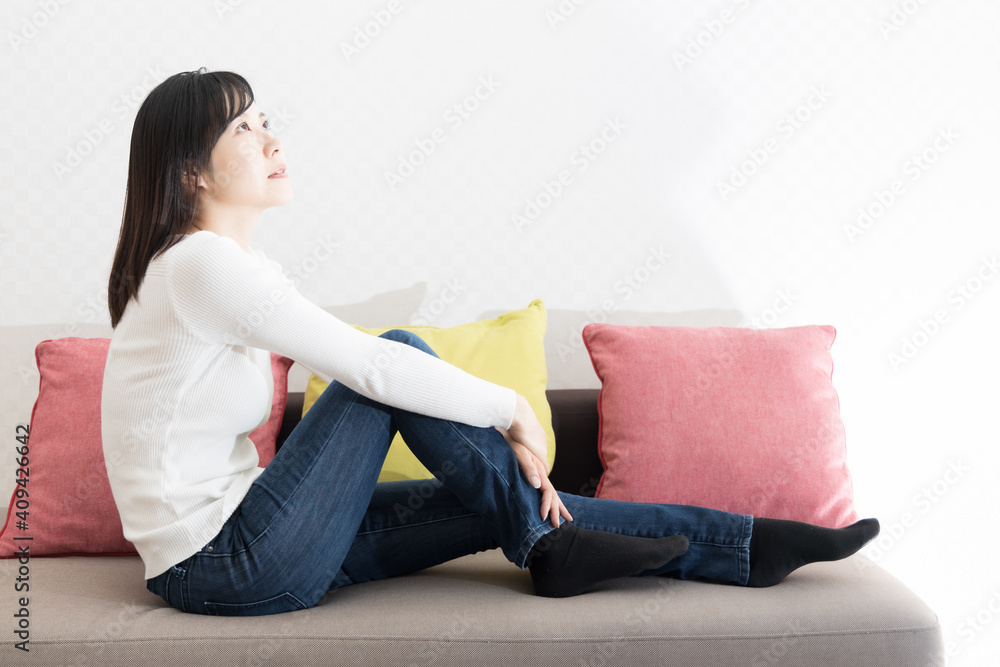 Woman sitting on the couch holding her knees Woman sitting on the couch holding her knees