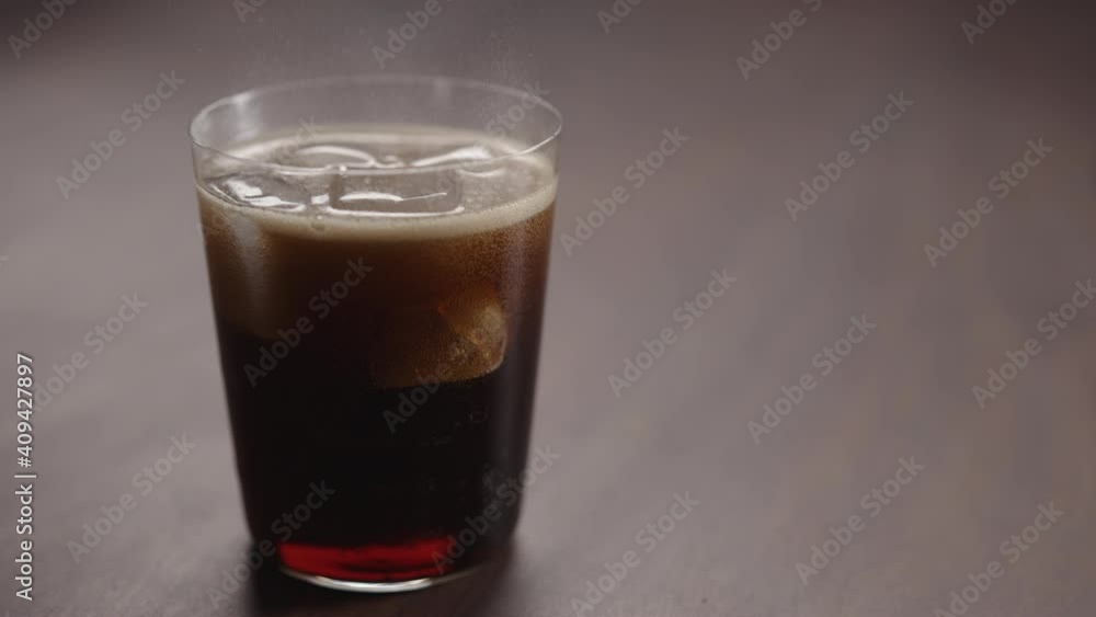 Slow motion man pour cola over ice cubes into tumbler glass on walnut table with copy space Slow motion man pour cola over ice cubes into tumbler glass on walnut table with copy space