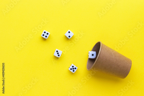 Gaming dice and cardboard cup on yellow background. Playing cube with numbers. Items for board games. Flat lay, top view with copy space.