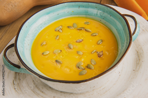 pumpkin soup with seeds in a beautiful plate on the background of the table and chopped pieces of pumpkin