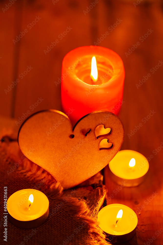 Fototapeta premium Wooden heart and candles on burlap and wooden boards. St Valentine's day greeting card with candle and heart on a blurred background. Love story concept