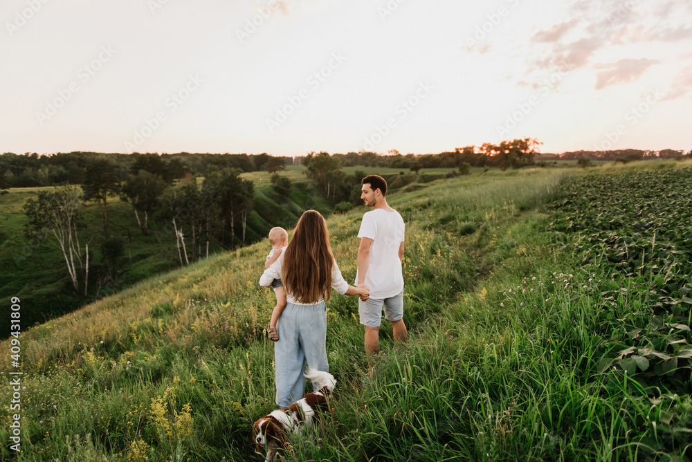 Young beautiful family with a little daughter and a dog hug, kiss and walk in nature at sunset. Young beautiful family with a little daughter and a dog hug, kiss and walk in nature at sunset.