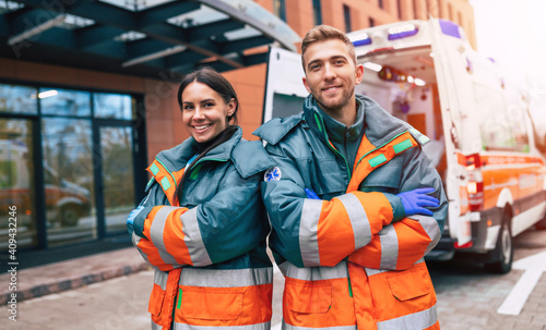 Two confident young doctors looking on the camera on ambulance and hospital background photo