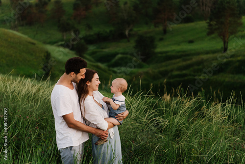 Young beautiful family with a little daughter hug, kiss and walk in nature. Photo of a family with a small child in nature.