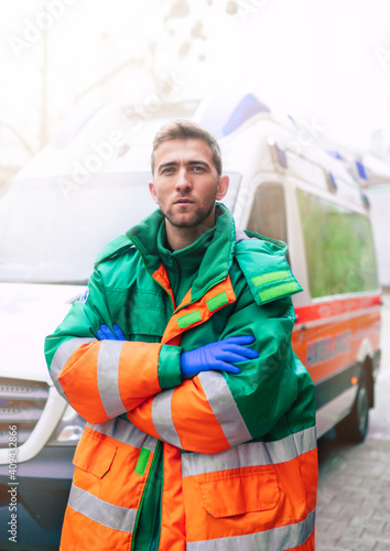 Professional and confident young man doctor looking on the camera with ambulance background