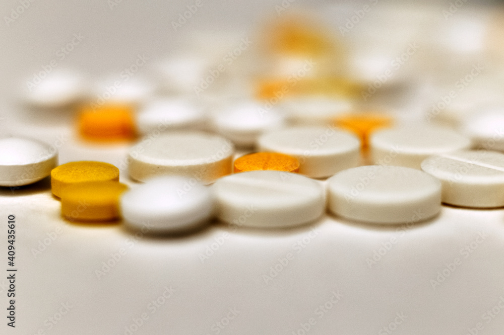 A sprinkle of yellow and white tablets, close-up front view. Blurred background. Medicines are out of focus. Medical background. Antibiotics A sprinkle of yellow and white tablets, close-up front view. Blurred background. Medicines are out of focus. Medical background. Antibiotics