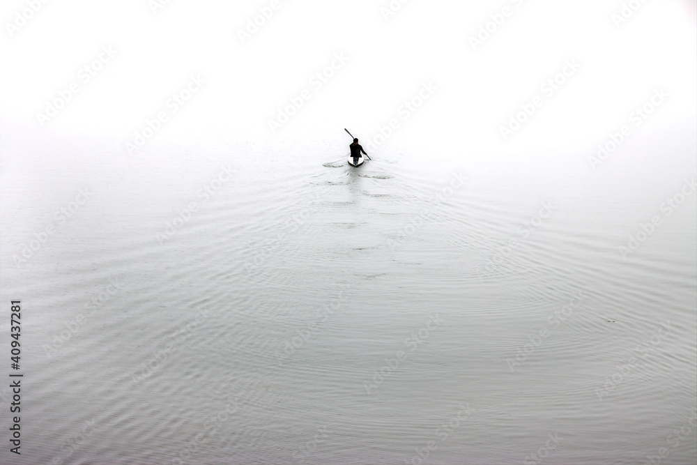 Fototapeta premium High key image of a silhouette of a man rowing a canoe. Minimalist photography concept