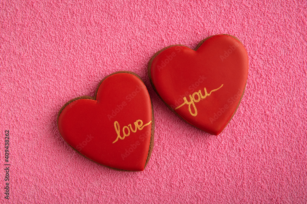 Two red cookies in shape of hearts with the inscription LOVE YOU on pink background. Two red cookies in shape of hearts with the inscription LOVE YOU on pink background.