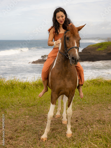 Asian woman riding horse near the ocean. Outdoor activities. Traveling concept. Vertical layout. Bali