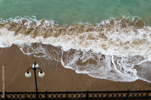 Fototapeta Naklejka Na Ścianę i Meble -  sea promenade with lantern and sand beach in stormy weather with waves
