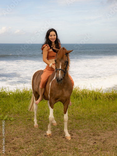 Smiling woman riding horse near the ocean. Outdoor activities. Human and animals relationship. Traveling concept. Copy space. Bali