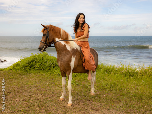 Smiling woman riding horse near the ocean. Outdoor activities. Love to animals. Traveling concept. Copy space. Bali