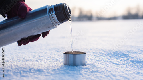 Pouring hot water frm thermos to cup in winter, winter sunrise or sunset, very cold weather, visible steam photo