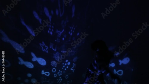 Little Asian boy in his room with night light projecting stars on room ceiling. Children read before bedtime.