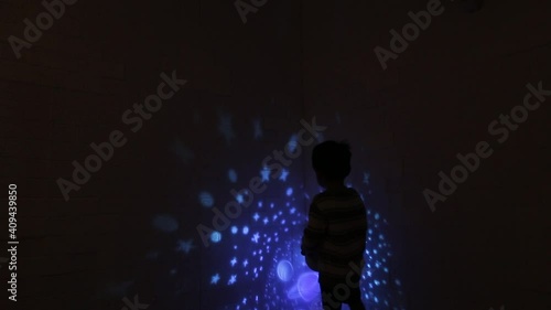 Little Asian boy in his room with night light projecting stars on room ceiling. Children read before bedtime.