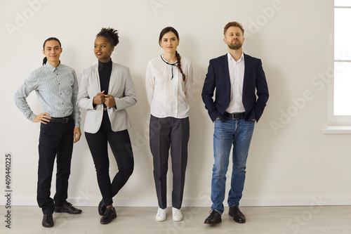 Full length group of young diverse office workers or job candidates. Full body team of different multiracial business people in formal and smart casual wear waiting near wall looking away or at camera photo