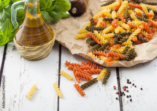 Raw homemade tricolore fusilli pasta in brown paper on white wooden background with basil and oil. photo