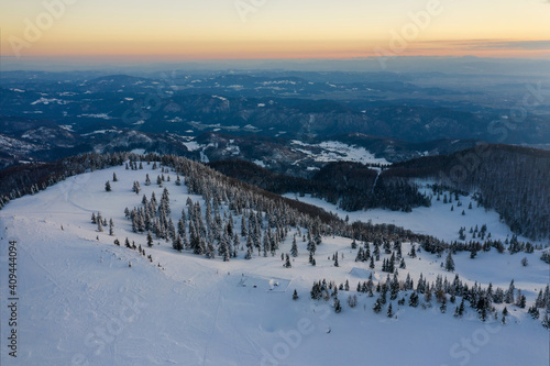 Aerial view of winter landscape with snow covered spruce forest in the mountains with beautiful sun light.