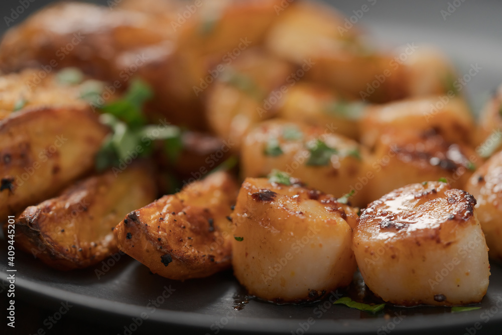 Seared scallops fith roasted potatoes on black plate closeup Seared scallops fith roasted potatoes on black plate closeup
