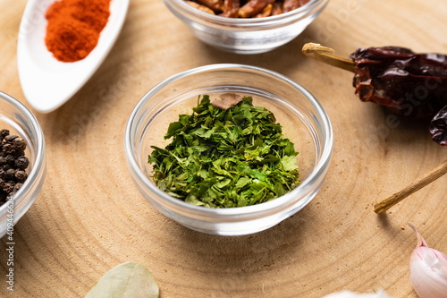 Chopped parsley in glass bowl on wood with other spices