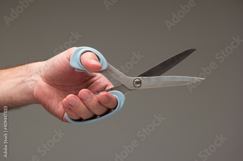 Caucasian male hand holding a special scissors made for left-handed people isolated on gray background photo