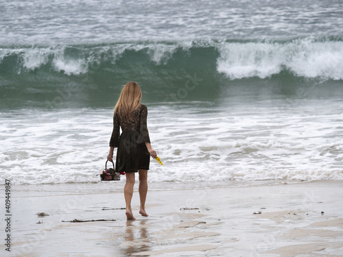 Back view of a female with a flower basket walking along the wavy seashore photo