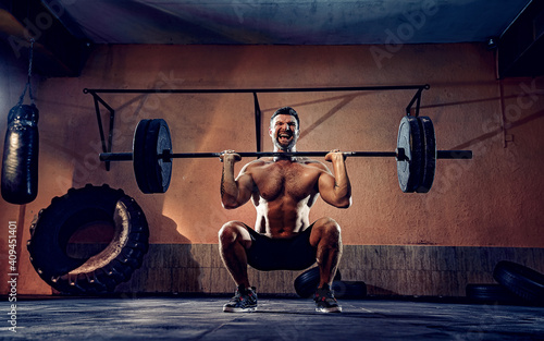 Muscular fitness man doing push a barbell over his head in his garage, selfisolation. Functional training. Snatch exercise. photo