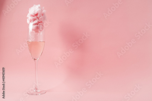 Glass of champagne with cotton candy on pink background
