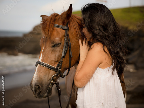 Portrait of Asian woman and brown horse. Woman hugging and kissing horse. Romantic concept. Human and animals relationship. Nature concept. Bali © Olga