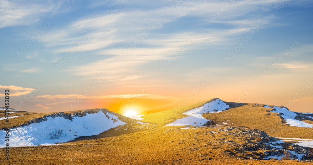 grass hill with melting snow at the sunset, spring outdoor evening scene