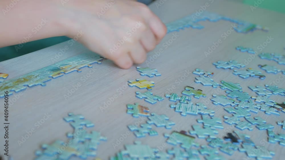 The puzzle lies on a light table. A child dressed in blue, with his right hand, slowly attaches the puzzle pieces to each other, in the correct position. Puzzle game, preschool education. The puzzle lies on a light table. A child dressed in blue, with his right hand, slowly attaches the puzzle pieces to each other, in the correct position. Puzzle game, preschool education.