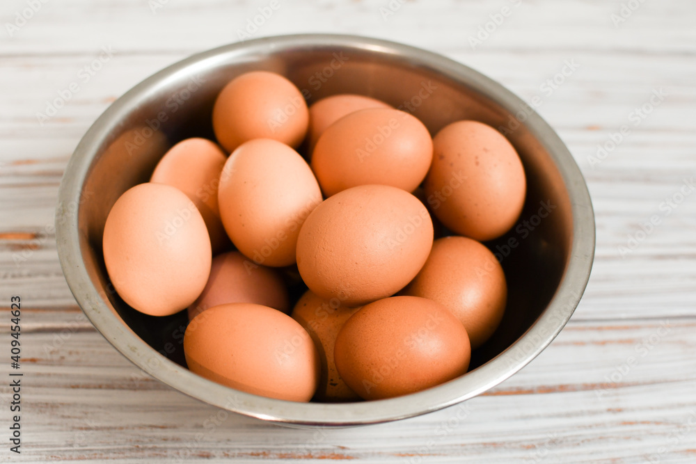Fresh chicken eggs in a metal bowl on a light wood background. Village. Organic farm product concept. Fresh chicken eggs in a metal bowl on a light wood background. Village. Organic farm product concept.